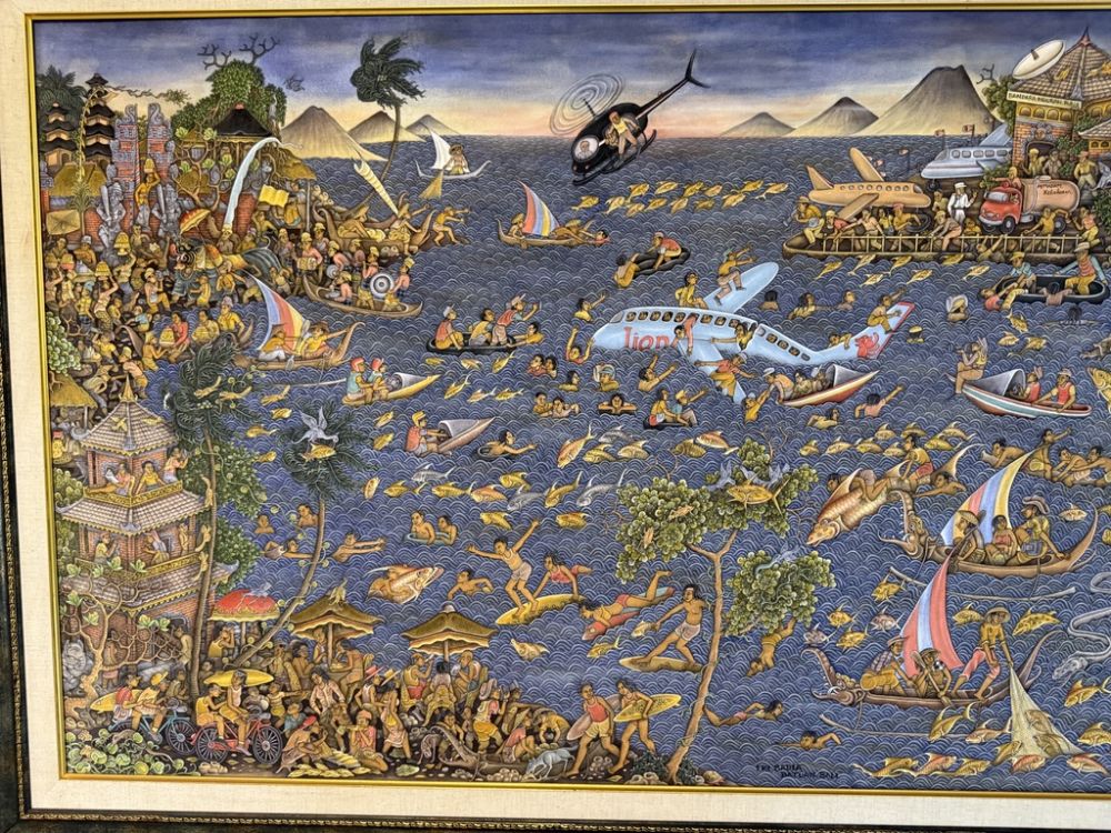 This piece depicts, in typical Bali art style, a plane crash from the 1990s!